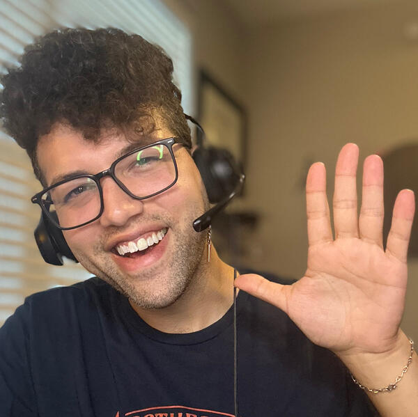Teacher Marcos Outline of friendly ESL teacher wearing glasses and a headset smiles and waves at the camera during an online lesson.
